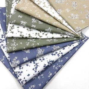 May include: A selection of fabric samples in shades of blue, green, and beige. Each piece displays a white floral design. The fabrics are arranged in a fan shape, highlighting the variety of patterns and colours available.
