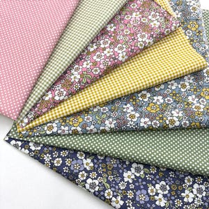 May include: A collection of fabric swatches in various patterns and colors. The fabrics include pink polka dots, green gingham, floral prints in pink and blue, yellow gingham, and a dark blue floral design. The swatches are arranged in a fan shape.