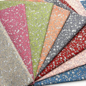 May include: A collection of fabric swatches in various colors, including pink, green, orange, gray, red, and blue. Each swatch is patterned with small white floral designs, creating a delicate and textured appearance. Ideal for sewing and crafting projects.