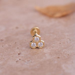 May include: Gold body jewelry with a hexagonal design and three clear cubic zirconia stones.
