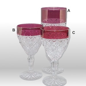 May include: Three clear glass goblets with a cut glass design. The goblets have a red rim. The goblet on the left is smaller than the other two. The goblet on the right is the largest.