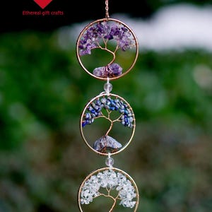 May include: A hanging wind chime with three circular frames, each with a wire tree design and different gemstones: purple, blue, and clear. The frames are suspended by a chain. The text "Ethereal gift crafts" is visible.
