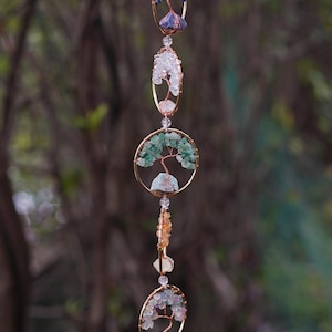 May include: A hanging ornament with gold-coloured circular and oval frames. Each frame features a wire tree design decorated with colourful gemstones. The gemstones include purple, blue, green, and red hues. The ornament hangs from a delicate chain.