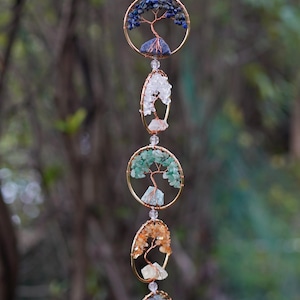 May include: A decorative hanging ornament with multiple circular and oval frames, each holding a wire tree design embellished with colourful gemstones. Gemstones include purple, blue, white, green, orange, and red. The frames are linked by a delicate chain.