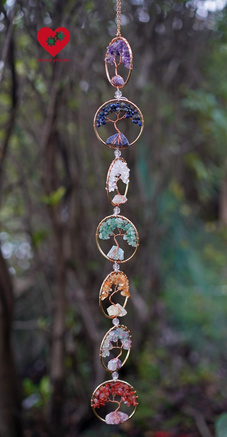 May include: A decorative hanging ornament with multiple circular and oval frames, each holding a wire tree design embellished with colourful gemstones. Gemstones include purple, blue, white, green, orange, and red. The frames are linked by a delicate chain.