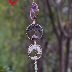 May include: A handcrafted wind chime with three circular and oval frames, each with a wire tree design and filled with amethyst, blue, and clear crystals. The chime is suspended by a gold chain.