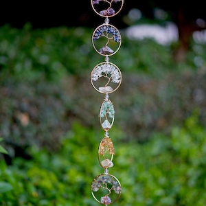May include: A decorative hanging ornament with gold-coloured circular and oval frames, each holding a wire tree design filled with colourful gemstones. The piece hangs from a delicate chain, with the text "Ethereal gift crafts" in the upper left corner.