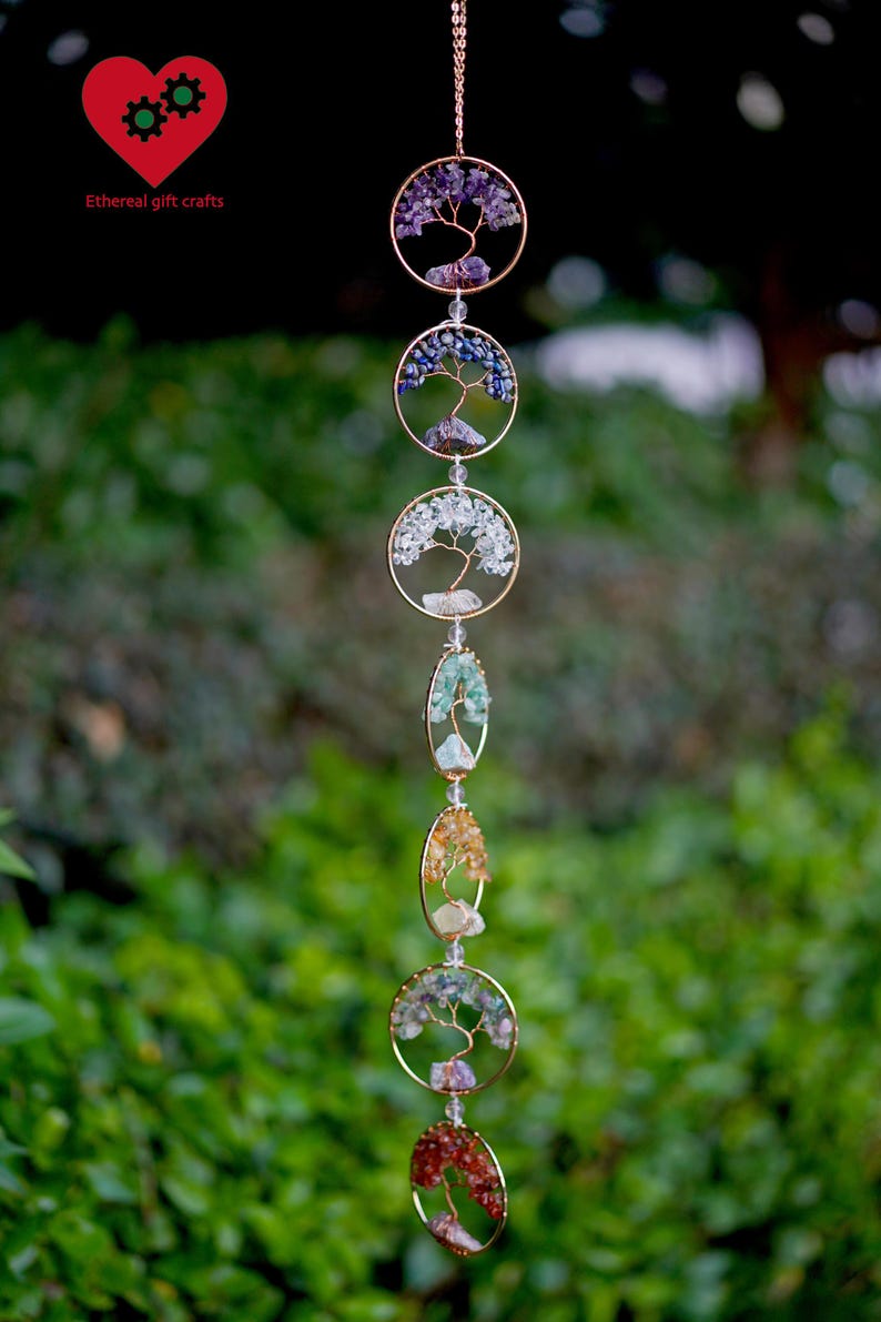 May include: A decorative hanging ornament with gold-coloured circular and oval frames, each holding a wire tree design filled with colourful gemstones. The piece hangs from a delicate chain, with the text "Ethereal gift crafts" in the upper left corner.