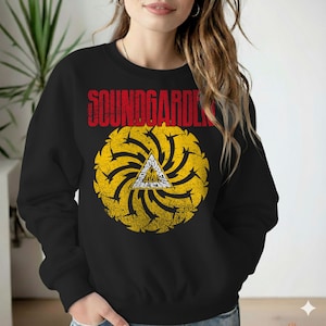 May include: Black sweatshirt featuring the band name "SOUNDGARDEN" in red block letters above a yellow and white graphic. The graphic is a circular design with a central triangle.