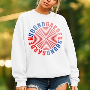 May include: White sweatshirt with a circular graphic that reads "SOUNDGARDEN" in red and blue lettering. The graphic features a spiral design in the center. The sweatshirt is paired with denim shorts.