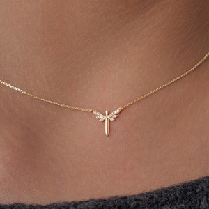 May include: A delicate gold chain necklace with a small dragonfly pendant adorned with tiny clear stones.