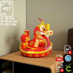 Puede incluir: Un modelo de papel de serpiente rojo y dorado con una linterna en la boca. La serpiente est&aacute; enroscada en un c&iacute;rculo y tiene una cara de dibujos animados. El modelo mide aproximadamente 40 cm de alto, ancho y profundidad.