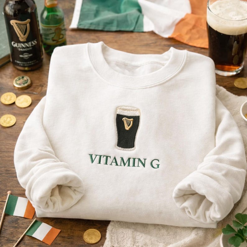 May include: Cream-colored sweatshirt with a black and gold embroidered pint of stout and the words "VITAMIN G" in green. The image includes Irish flags, coins, and bottles of Guinness.