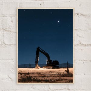 Op de afbeelding: Een ingelijste verticale print met het donkere silhouet van een graafmachine in een woestijnlandschap bij nacht. De grond is verlicht met warm licht, wat contrasteert met de diepblauwe sterrenhemel en de verre bergen op de achtergrond.