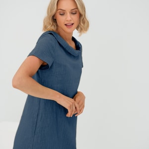 May include: A woman wearing a short-sleeved, blue linen dress with a collar. The dress has a relaxed fit and a slightly A-line silhouette.
