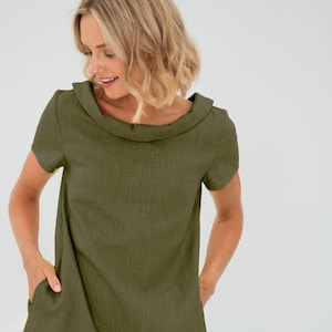 Könnte beinhalten: Ein schlichtes, olivgrünes Leinenkleid mit einem breiten, gefalteten Kragen und kurzen Ärmeln. Das Kleid hat zwei Taschen auf der Vorderseite.