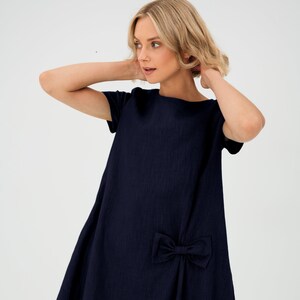 Könnte beinhalten: Ein dunkelblaues Kleid mit kurzen Ärmeln und einem Schleifendetail an der Seite.