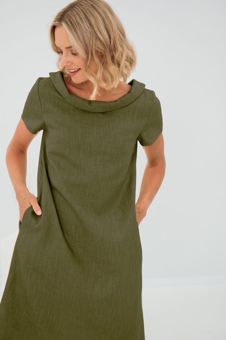 May include: A simple, olive green linen dress with a wide, folded collar and short sleeves. The dress has a relaxed fit and features two pockets on the front.