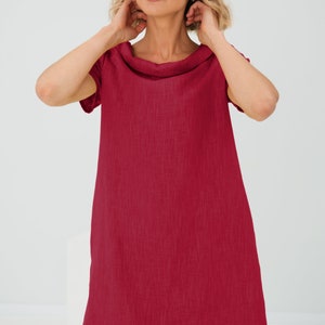 May include: A short-sleeved, knee-length dress in a vibrant red hue. The dress features a cowl neckline and a relaxed, A-line silhouette. The fabric appears to be a lightweight linen or similar material, ideal for warmer weather. The dress is a solid color with no visible patterns.