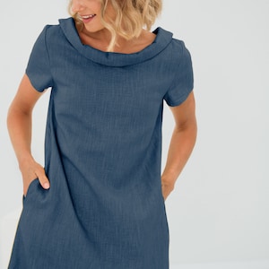 May include: A dark blue linen dress with a cowl neck and short sleeves. The dress has two pockets on the front.