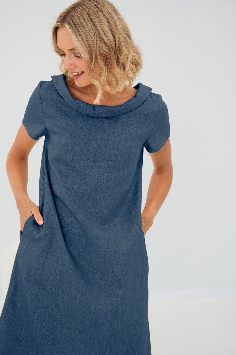 May include: A dark blue linen dress with a cowl neck and short sleeves. The dress has two pockets on the front.