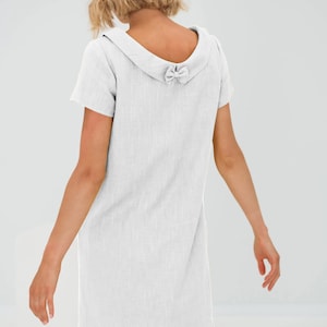 May include: A white linen dress with a short sleeve and a bow detail on the back of the collar.
