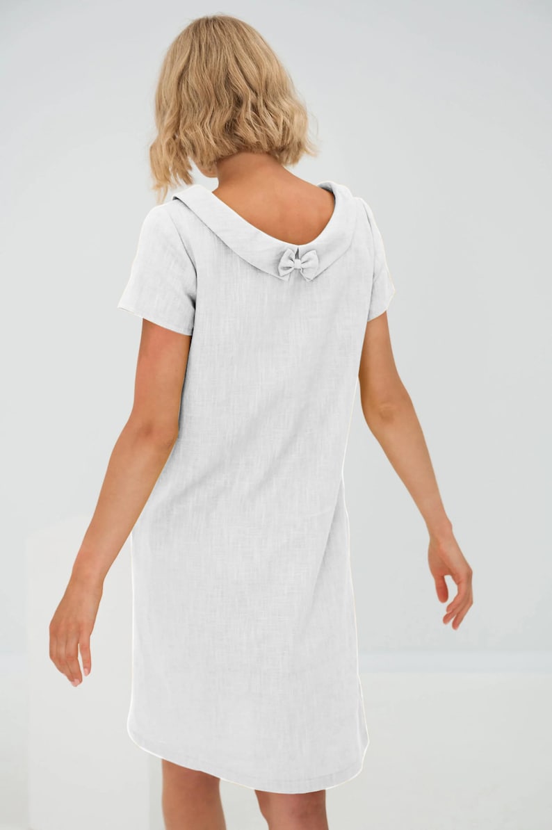 May include: A white linen dress with a short sleeve and a bow detail on the back of the collar.