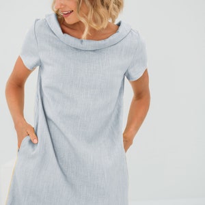 May include: A light blue linen dress with a cowl neck and short sleeves. The dress has pockets on the sides and a subtle texture.
