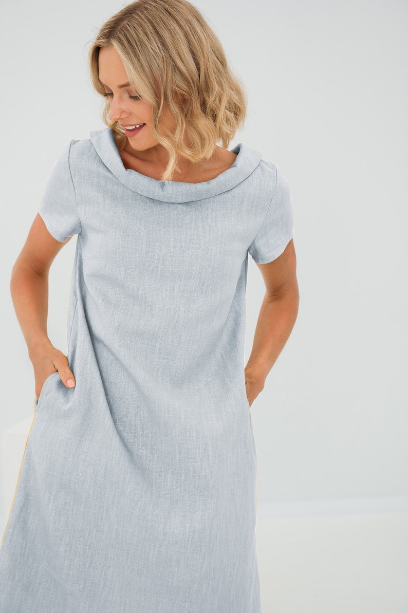 May include: A light blue linen dress with a cowl neck and short sleeves. The dress has pockets on the sides and a subtle texture.