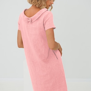 May include: A pink linen dress with a large collar and a bow detail on the back. The dress has short sleeves and a straight silhouette.