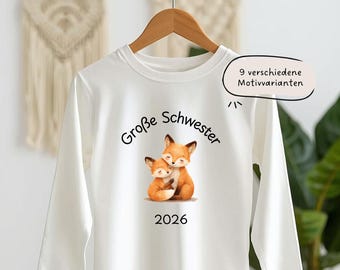 Pode incluir: Camiseta branca de manga comprida com um gráfico de duas raposas abraçadas em tons de laranja e castanho. O texto "Große Schwester" e "2026" estão impressos na camiseta. Um balão de fala diz "9 verschiedene Motivvarianten".