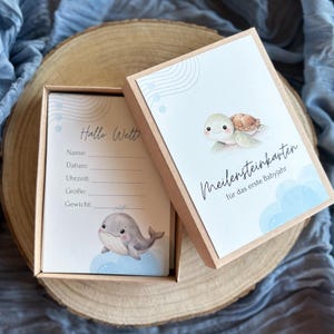 Può includere: Un set di biglietti per le tappe fondamentali del bambino in una scatola. La scatola e i biglietti presentano illustrazioni di una balena e una tartaruga. I biglietti hanno sezioni da compilare per il nome, la data, l'ora, la taglia e il peso del bambino.