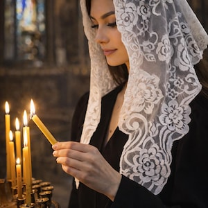 Peut inclure: Une femme portant un voile de dentelle blanche &agrave; motifs floraux, tenant une bougie allum&eacute;e pr&egrave;s d'un groupe de bougies allum&eacute;es. Les bougies sont jaunes et plac&eacute;es dans un support en laiton d&eacute;coratif. La femme porte un v&ecirc;tement noir.