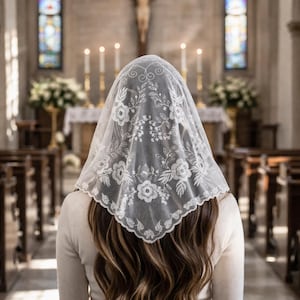 Puede incluir: Una persona con un velo de encaje blanco con bordados florales, sentada en una iglesia. La persona está frente al altar, con un crucifijo y velas en el fondo. La iglesia tiene vidrieras y bancos de madera.