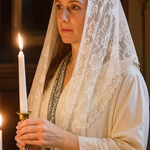 Pu&ograve; includere: Una donna con un velo di pizzo bianco tiene in mano una candela bianca accesa in un candelabro dorato. La donna indossa un abito color crema. La scena &egrave; illuminata in modo soffuso, suggerendo un contesto religioso o cerimoniale.