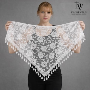 Pu&ograve; includere: Una mantilla di pizzo bianco con un motivo floreale a rose e un bordo smerlato con dettagli a goccia. Il logo Divine Veils &egrave; visibile in alto a destra. La mantilla &egrave; tenuta da una persona.