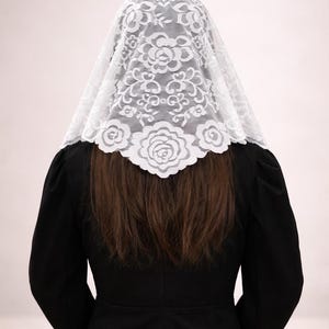 Peut inclure: Un voile en dentelle blanche orn&eacute; d'un motif floral, port&eacute; sur la t&ecirc;te et les &eacute;paules. Le voile est fait de dentelle d&eacute;licate et est associ&eacute; &agrave; un v&ecirc;tement noir. L'image est prise de dos, montrant le design complexe du voile.