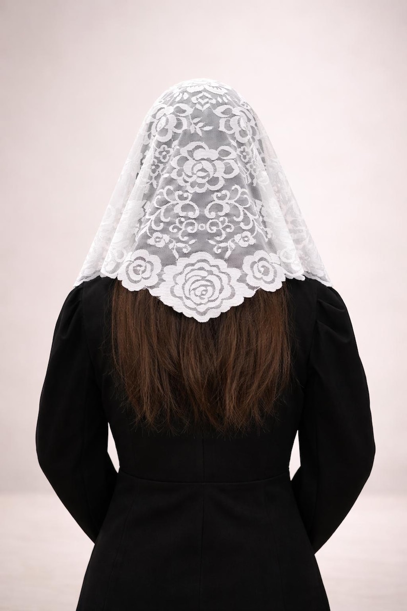 Peut inclure: Un voile en dentelle blanche orn&eacute; d'un motif floral, port&eacute; sur la t&ecirc;te et les &eacute;paules. Le voile est fait de dentelle d&eacute;licate et est associ&eacute; &agrave; un v&ecirc;tement noir. L'image est prise de dos, montrant le design complexe du voile.