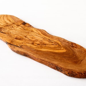 May include: An olive wood serving board with a natural, irregular shape. The board displays a warm brown hue with detailed grain patterns. The edges have a rustic, unfinished appearance, adding to its unique character.