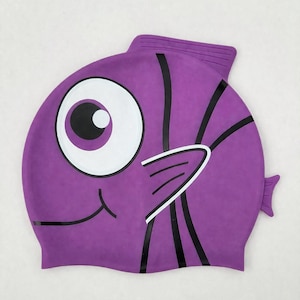 May include: A purple swim cap with a cartoon fish design. The cap features a large white and black eye, black stripes, and a smiling mouth. The cap is made of a flexible material and is designed to fit snugly on the head.