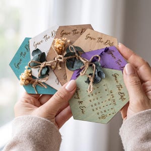 Könnte beinhalten: Eine Sammlung sechseckiger Save-the-Date-Karten aus Holz in verschiedenen Farben wie Türkis, Weiß, Naturholz, Lila und Hellgrün. Jede Karte zeigt den Text Save the Date, einen Kalender und ist mit Trockenblumen und einer Paketschnur verziert.