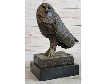 May include: Bronze owl sculpture with detailed feather textures, perched on a textured base atop a black marble pedestal. The owl is depicted in a lifelike pose, showcasing its distinctive facial features.