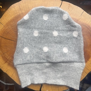 May include: A gray beanie with white polka dots. The hat is made of a soft, knitted material and has a ribbed cuff. The beanie is shown on a wooden surface.