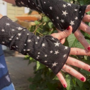 May include: A pair of black arm warmers featuring a repeating pattern of small white stars. These fingerless sleeves are crafted from a soft knit fabric and extend from the wrist to the mid-forearm, providing coverage while leaving the fingers free.