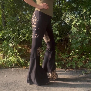 May include: Black bell-bottom pants featuring solid black panels contrasted with sections of tan and black leopard print fabric. The pants have a high-waisted fit and a flared leg silhouette that widens significantly toward the bottom hem.