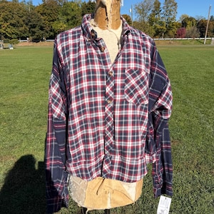 May include: A long-sleeve button-down shirt featuring a red, white, and navy blue plaid pattern. The garment has a pointed collar, a single chest pocket on the left side, and a straight hemline. The fabric displays a mix of plaid panels.