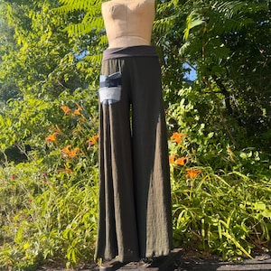 May include: Olive green wide-leg pants featuring a high-rise waistband and a single patch pocket on the right hip. The pocket is constructed from two distinct shades of blue denim fabric, creating a contrasting rectangular detail on the solid pants.