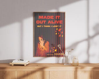 Pode incluir: Um pôster emoldurado com fundo vermelho e preto. O pôster apresenta uma pessoa com a cabeça nas mãos e o texto "MADE IT OUT ALIVE BUT I THINK I LOST IT". O pôster também apresenta uma cortina vermelha e estrelas amarelas.