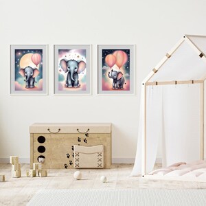 Puede incluir: Tres impresiones enmarcadas de lindos elefantes de dibujos animados con globos rosas y azules. Los elefantes est&aacute;n volando en el cielo con estrellas y una luna en el fondo. Las impresiones est&aacute;n en marcos blancos y est&aacute;n colgadas en una pared blanca.