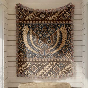 May include: A rectangular woven throw blanket featuring a central symmetrical bird motif with spread wings in shades of brown, cream, and dark blue. The design includes intricate floral and geometric patterns with a fringed edge on all sides.